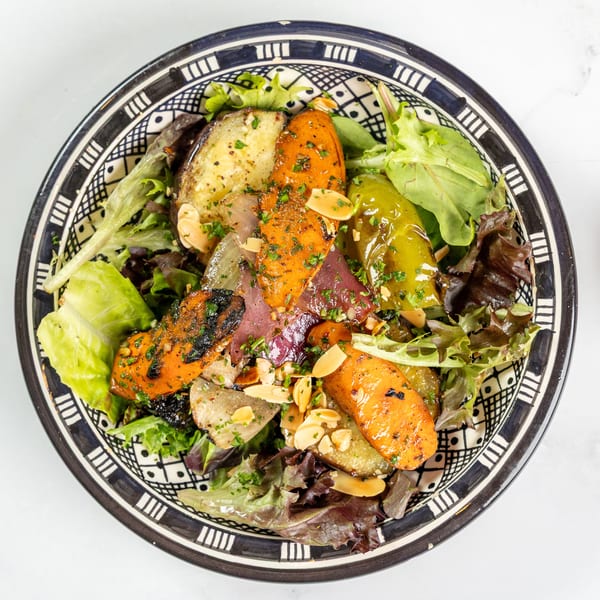Overhead view of a colorful salad with roasted vegetables, greens, and sliced almonds in a decorative bowl.