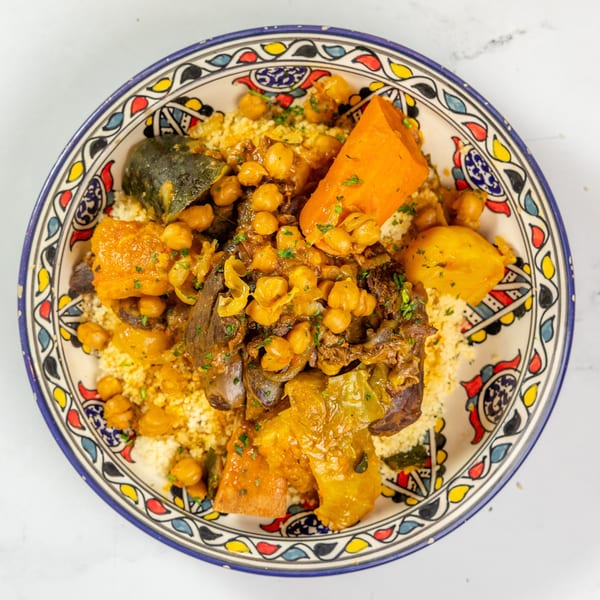 Couscous with chickpeas, meat, and vegetables in a colorful, patterned bowl on a white surface.