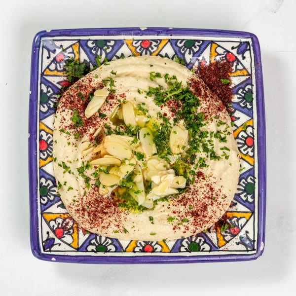 Creamy hummus topped with sliced garlic, parsley, sumac, and olive oil on a decorative plate.