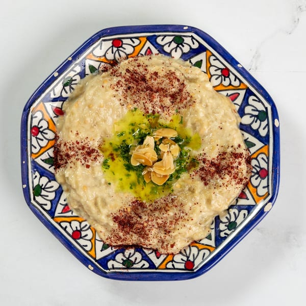 Creamy baba ghanoush topped with olive oil, parsley, almonds, and sumac in a decorative blue bowl.
