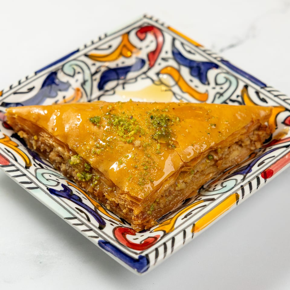 A triangular piece of baklava, drizzled with honey and sprinkled with pistachios, on a colorful plate.