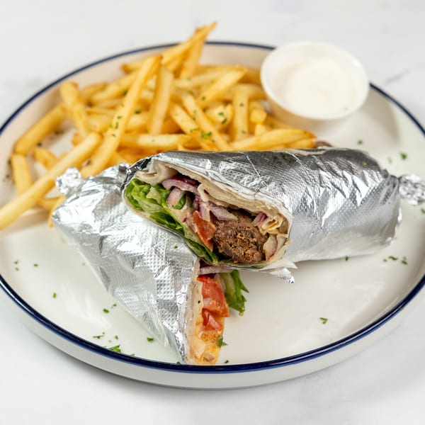Two foil-wrapped shawarma wraps with fries and a side of white sauce on a white plate.