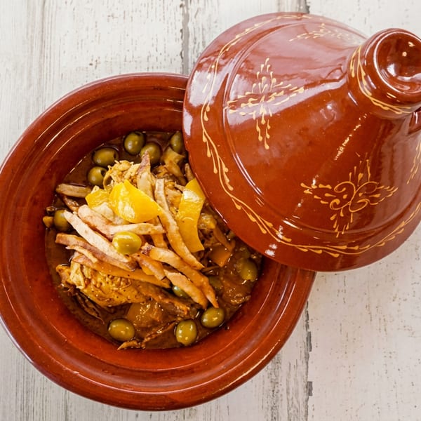 Moroccan chicken tagine with olives, preserved lemons, and fries in a traditional clay pot.