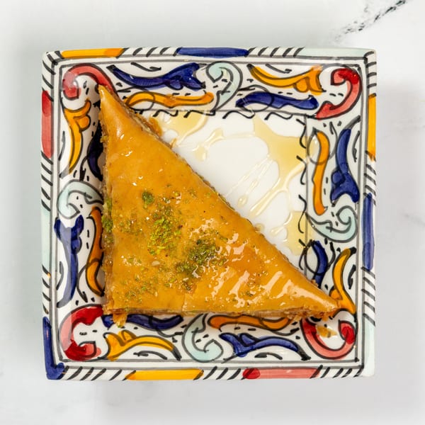 A triangular piece of baklava drizzled with honey and sprinkled with pistachios on a colorful plate.