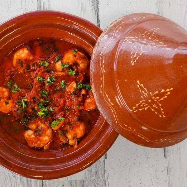 Shrimp tagine with red sauce and parsley in a terracotta dish with its lid.