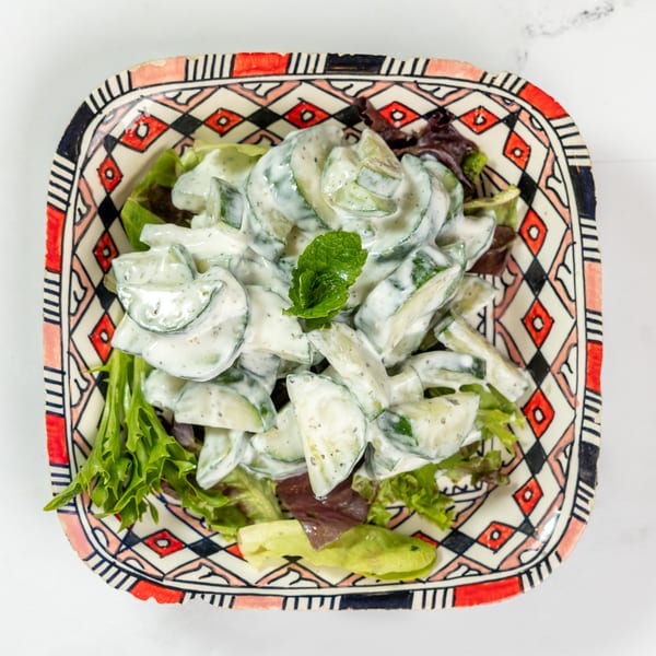 Cucumber salad with creamy dressing and a mint garnish, served in a colorful patterned bowl.