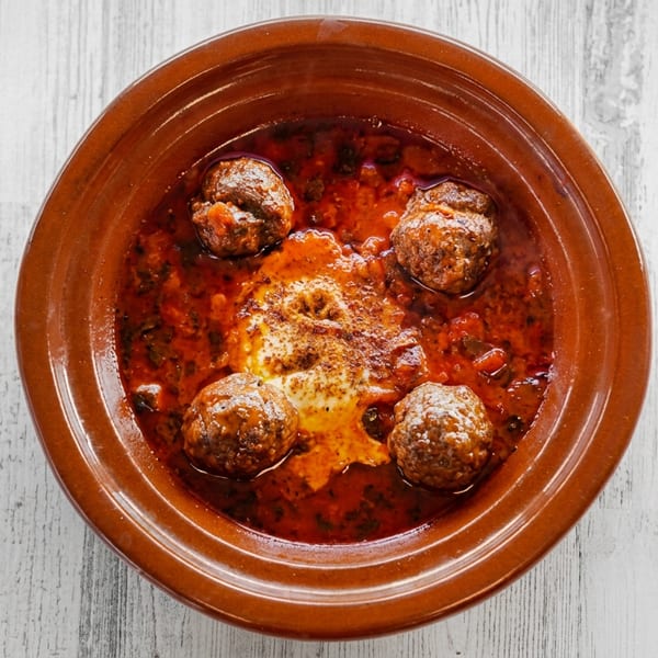 Meatballs in a rich red sauce with a dollop of cream, served in a rustic brown bowl.